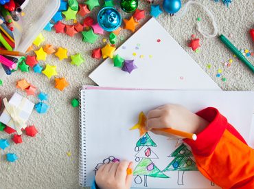 Child's hands drawing a Christmas scene with crafting all around
