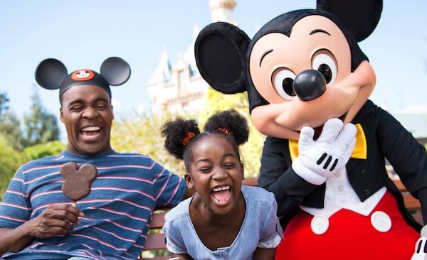 Mickey Mouse laughing to camera with little girl with mouse ear styled hair and dad wearing mouse ear hat