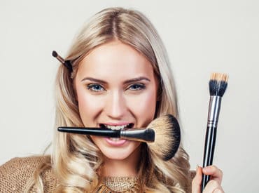 Lady in gold holding up and biting make up brushes